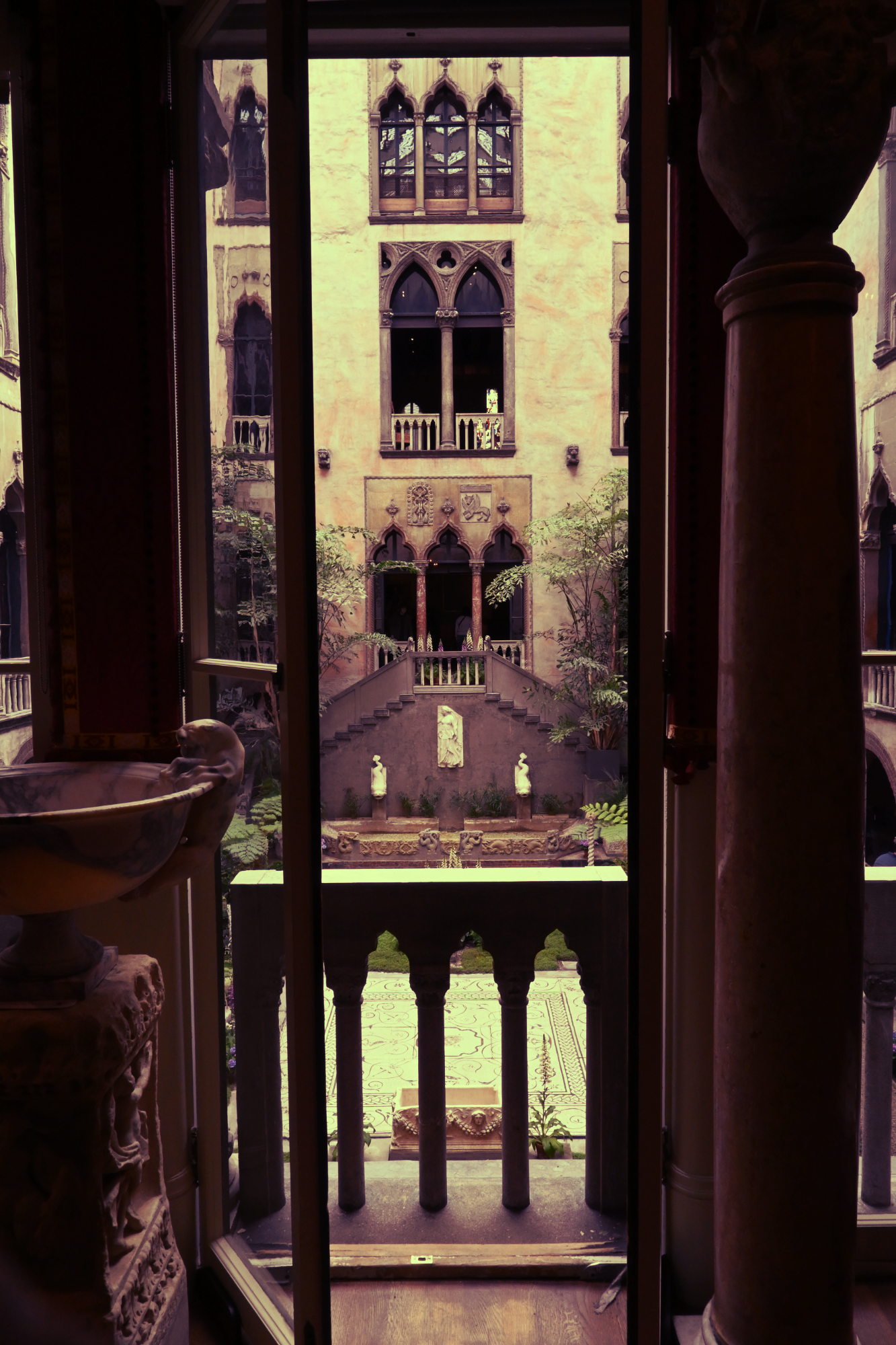 The courtyard of the isabella stewart gardnew museum, framed by an ope french door no the second floor.