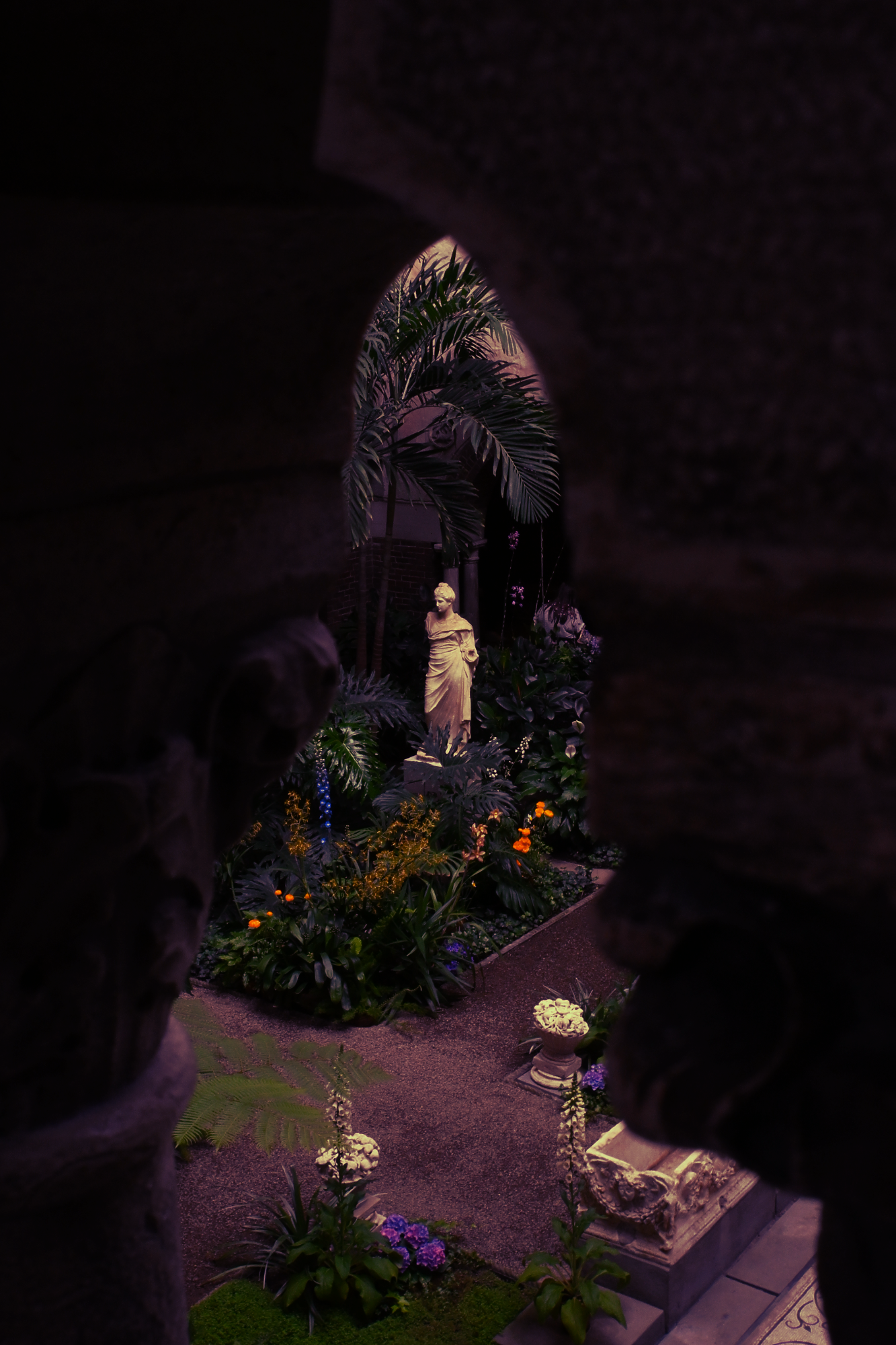 A marble statue of Persephone, surrounded by blooming flowers and framed by the marble balusters of the balcont above.