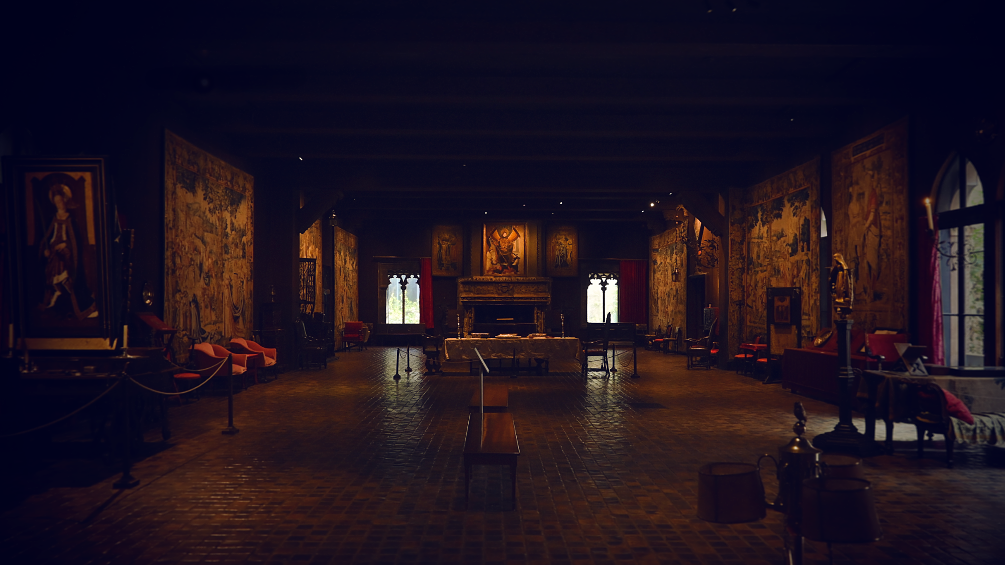 The tapestry room of the Gardner, dimly lit, with a large fireplace in the center and massive tapestries on the walls.